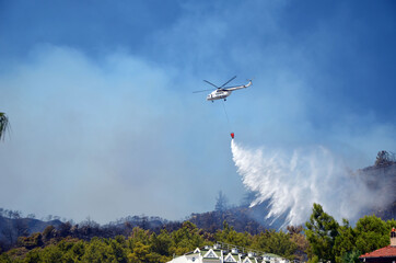 Fototapeta na wymiar Russian helicopter draws water from the sea to extinguish a forest fire. Marmaris,Turkey