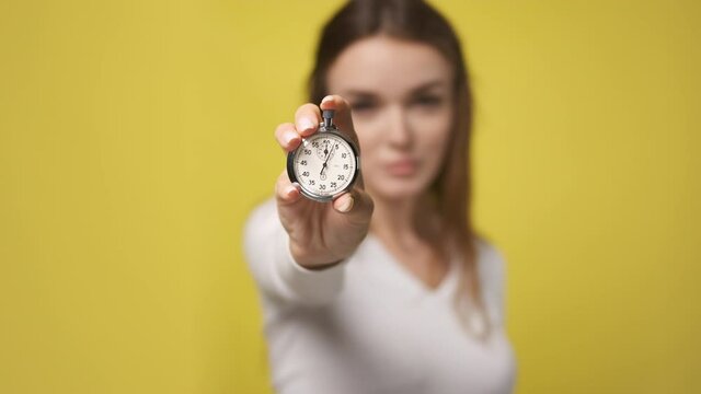 Stopwatch in foreground in hand of attractive young woman. stopwatch counts down from zero. Retro old vintage clock timer in hand of nice lady. little time left, clock is ticking. Yellow background