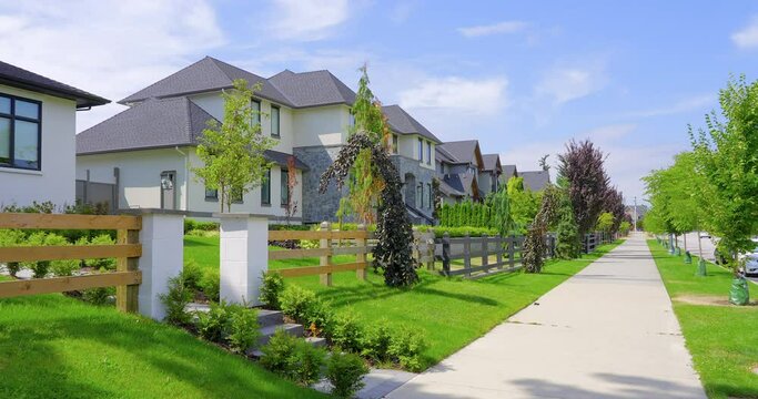 Establishing shot. Neighbourhood of luxury houses with street road, big trees and nice landscape in Vancouver, Canada. Blue sky. Day time on June 2021. Still camera view. ProRes 422 HQ.