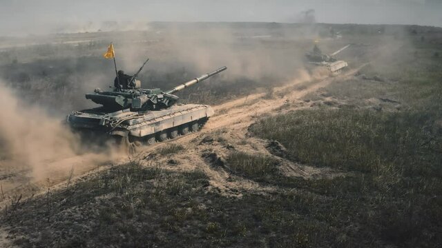 Many tanks with tankman driving dusty road. Aggressive military company. Tankers on alert. Demonstration strength. Invasion someone else's territory. Smoke from shots. Tracking drone flight
