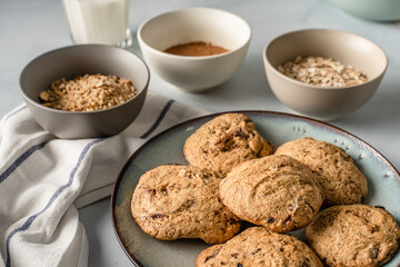 Close up front view on crunchy oatmeal chip cookies fresh baked biscuits with chocolate and cocoa in a plate on the table and ingredients beside homemade food concept