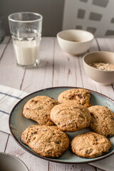 Close up front view on crunchy oatmeal chip cookies fresh baked biscuits with chocolate and cocoa in a plate on the table and ingredients beside homemade food concept