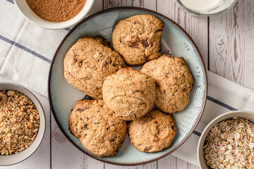 Close up top view on crunchy oatmeal chip cookies fresh baked biscuits with chocolate and cocoa in a plate on the table and ingredients beside homemade food concept