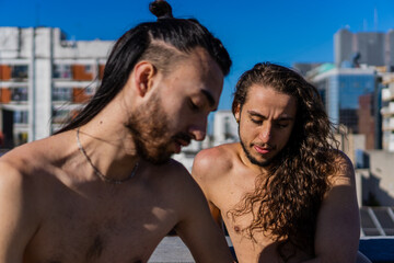 young brazilian man and long-haired hispanic latino man with shirtless long hair sunbathing on a terrace with a view, talking