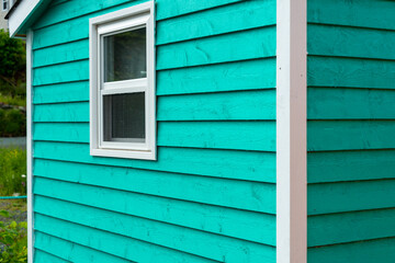 The exterior of a bright green narrow wooden horizontal clapboard wall of a house with one vinyl window. The trim on the glass panes is white in color. The outside boards are textured pine wood.  