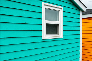 The exterior of a bright green narrow wooden horizontal clapboard wall of a house with one vinyl window. The trim on the glass panes is white in color. The outside boards are textured pine wood.  