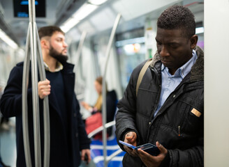 Focused African man absorbed in his smartphone while traveling in subway car