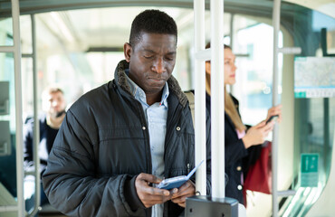 Fototapeta na wymiar African man browsing on his smartphone while traveling on modern city tram on winter day