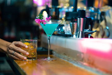 Bartender preparing tasty mixed alcoholic drink with ice cube in decorated cocktail glass on bar counter for customer in nightclub. Celebration party, nightlife business and alcohol addiction concept