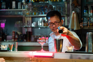 Bartender preparing tasty mixed alcoholic drink with ice cube in decorated cocktail glass on bar counter for customer in nightclub. Celebration party, nightlife business and alcohol addiction concept