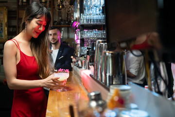 Asian woman sitting at bar counter drinking cocktail and talking to barman in nightclub. Male mixologist bartender preparing alcoholic drink to customer. Small business bar and city nightlife concept