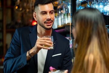 Asian woman talking to boyfriend with drinking alcoholic cocktail at bar counter in nightclub. Male bartender mixologist preparing mixed alcoholic drink with decorate cocktail glass at bar counter