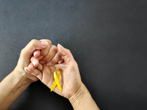 Celebration Day Concept - yellow ribbon on palm background. Symbolize the world suicide prevention day. Stock photo.