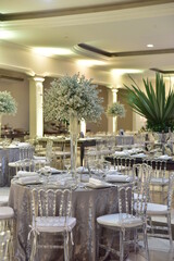 A luxurious bouquet of fresh flowers in a crystal vase on the table with cutlery plates and an elegant portion in the party restaurant with backlit and unfocused background.