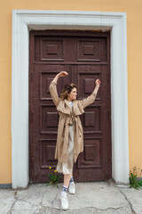 Fototapeta na wymiar Young millennial woman with wild hair dressed in an autumn coat posing near the door of an old building.