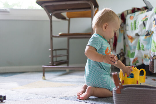 14 month old baby kneeling on the ground playing with school bus toy and figures