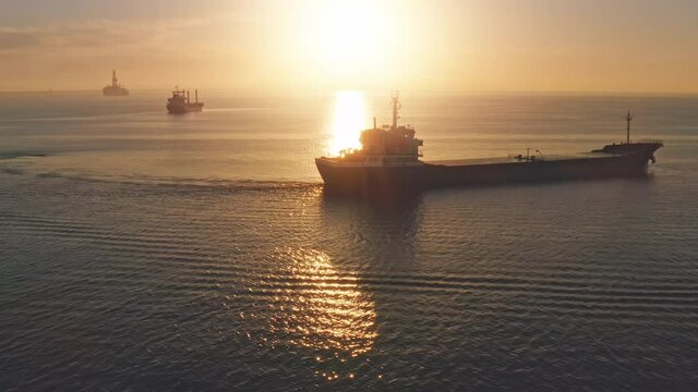 Dry cargo ships in orange sunset ocean. Aerial view oil gas station. International goods sea transportation. Export, import around world. Industrial business concept. Slow motion drone flight panorama