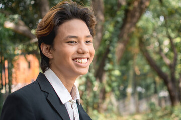 A happy teenage man of Filipino or Pacific Islander descent. In formal wear or university uniform....