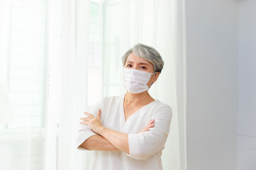 woman with gray hair wearing mask by the window