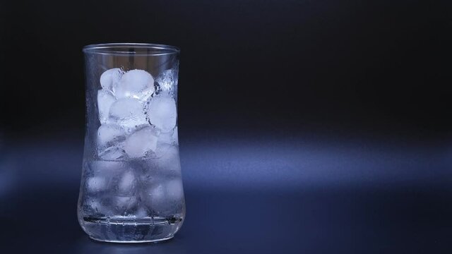 Close-up time-lapse video showing ice in clear glass of water melting on copy space black background as temperature rises. About global warming from world climate change and greenhouse effect.