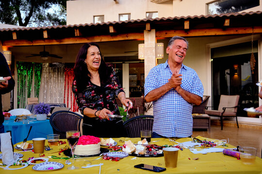 Elderly mature latinx latino and Latina Mexican man and woman couple cheering and laughing at a party cutting cake