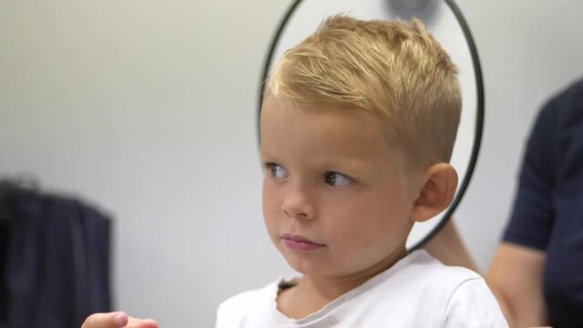 Young boy child sees his new blond hair haircut and smiles at barber saloon