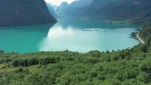 Green lush forest and glacier green freshwater lake in Olden Norway - Aerial flying over forest and approaching lake with mountain background