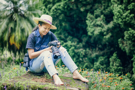Young girl nature photographer in hat sitting on stone looking photos on dslr camera