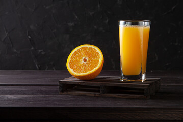 Orange fruit and glass of juice on dark wooden background