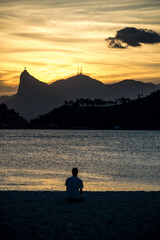 pessoa observa o por de sol  sobre o rio de janeiro e o corcovado na praia de niterói.