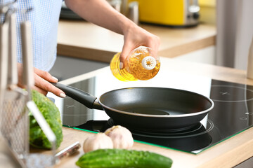 Young woman pouring oil into frying pan in kitchen