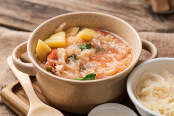 Pot with tasty sauerkraut soup on wooden background, closeup