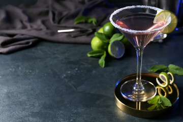 Glass of tasty cosmopolitan cocktail and limes on dark background