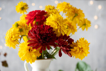 Bouquet of red and yellow flowers in jug against blurred fairy lights 