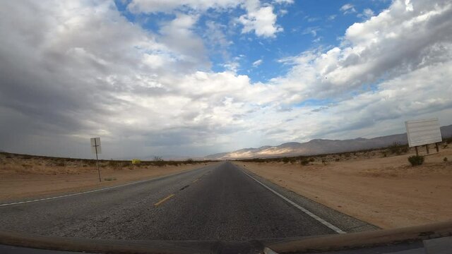 Driving through the Mojave Desert towards the distant mountains on a cloudy day - driver point of view