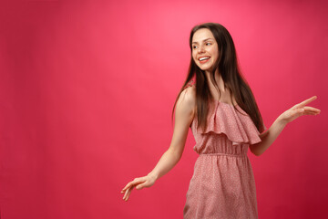 Young smiling woman dancing with arms outstretched against pink background