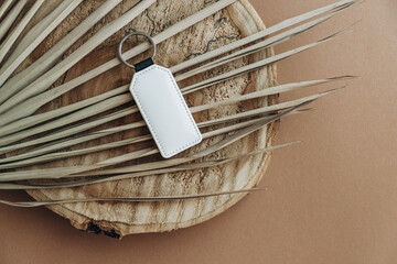 Keychain mockup among brown palm leaves to display design. Blank white sublimation key chain photo.