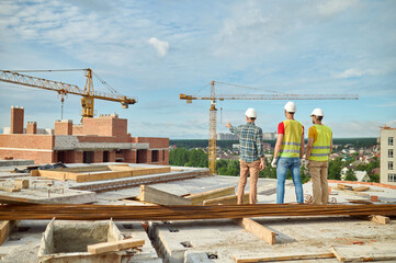 Three men in protective helmets inspecting the building site