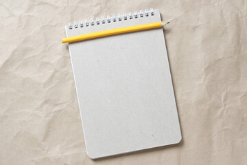 Gray notepad with white coiled spring and pencil on a background of beige crumpled craft paper. With empty space for text and design