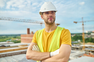 Calm attractive worker in cotton gloves and a hardhat looking away