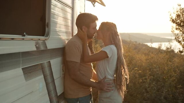 A lovely couple is kissing standing near caravan trailer outside
