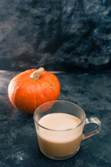 One pumpkin squash and a latte coffee made with with plant based oat soya or almond milk  with blank notepad notebook at the table on the dark black blue textured copy space background  work concept