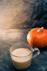 One pumpkin squash and a latte coffee made with with plant based oat soya or almond milk  with blank notepad notebook at the table on the dark black blue textured copy space background work concept