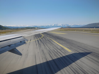 Fototapeta na wymiar Airplane wing takoff on runway with snow mountain background