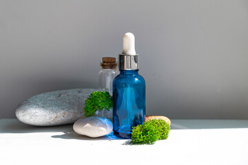 Sea moss personal care. Blue bottle with oil dropper and sea stones and moss on white background....