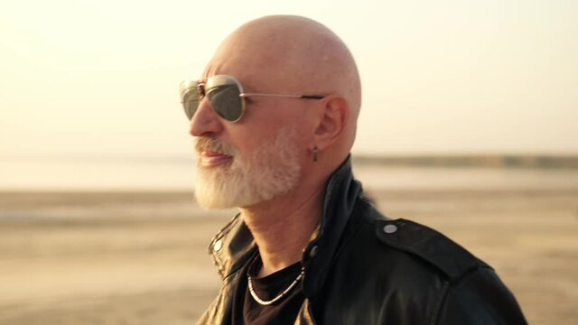 Close-up view of a handsome european biker man with beard wearing leather jacket walking outside near lake