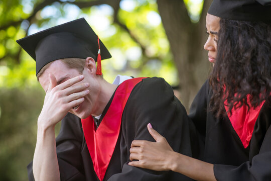 A cute girl in academic cap whispering something to her friend in the ear