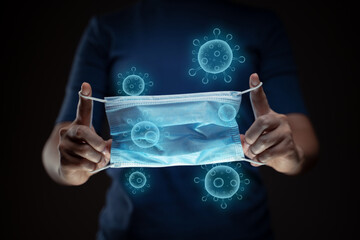 Close up shot of hands holding protective face mask with virus hologram effect.