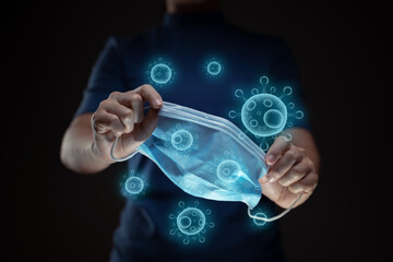 Close up shot of hands holding protective face mask with virus hologram effect.