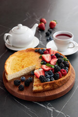 Pie with berries with a cut piece, with a cup of tea and teapot, strawberries, blackberries, blueberries